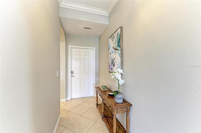 hall with light tile patterned floors, ornamental molding, visible vents, and baseboards