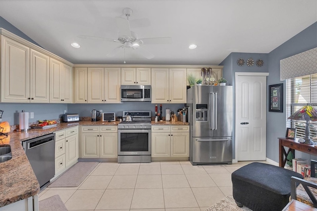 kitchen featuring light tile patterned floors, ceiling fan, stone counters, appliances with stainless steel finishes, and cream cabinets