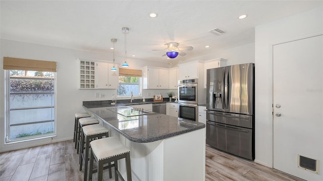 kitchen with sink, appliances with stainless steel finishes, kitchen peninsula, pendant lighting, and white cabinets