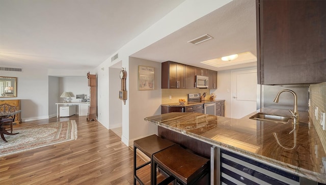 kitchen with appliances with stainless steel finishes, wood-type flooring, dark brown cabinetry, sink, and kitchen peninsula