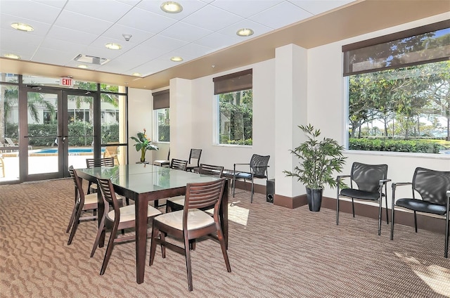 carpeted dining space with a healthy amount of sunlight, french doors, and a drop ceiling