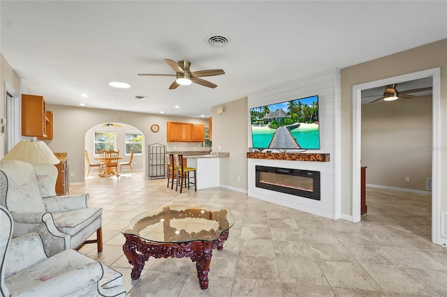 living room featuring visible vents, baseboards, arched walkways, ceiling fan, and a large fireplace