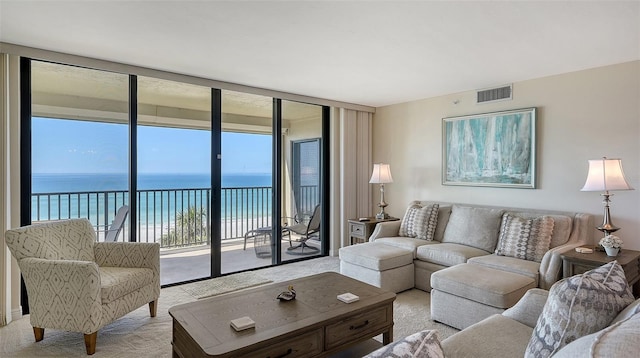 living room with a water view, light colored carpet, expansive windows, and a view of the beach