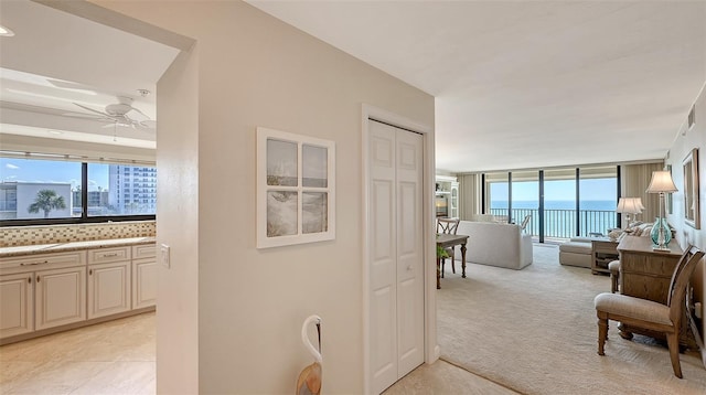 hall featuring a water view, a wall of windows, and light carpet