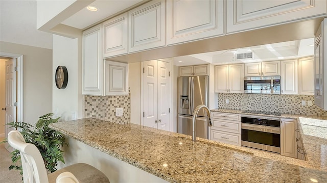 kitchen with sink, appliances with stainless steel finishes, backsplash, a kitchen breakfast bar, and light stone countertops