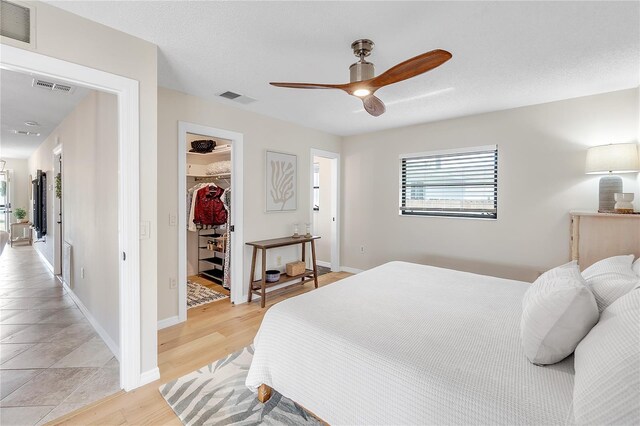 bedroom featuring light hardwood / wood-style flooring, ceiling fan, a textured ceiling, a spacious closet, and a closet