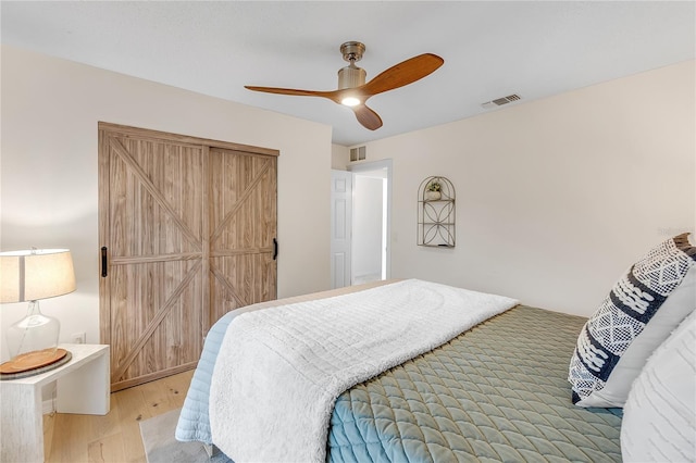 bedroom featuring ceiling fan, a barn door, and light wood-type flooring