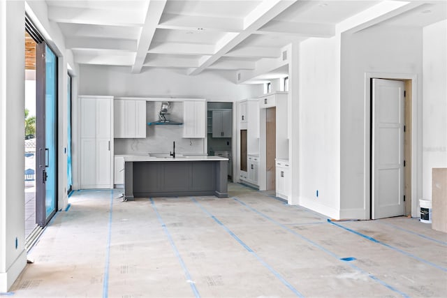 kitchen featuring coffered ceiling, beamed ceiling, a kitchen island with sink, decorative backsplash, and wall chimney range hood