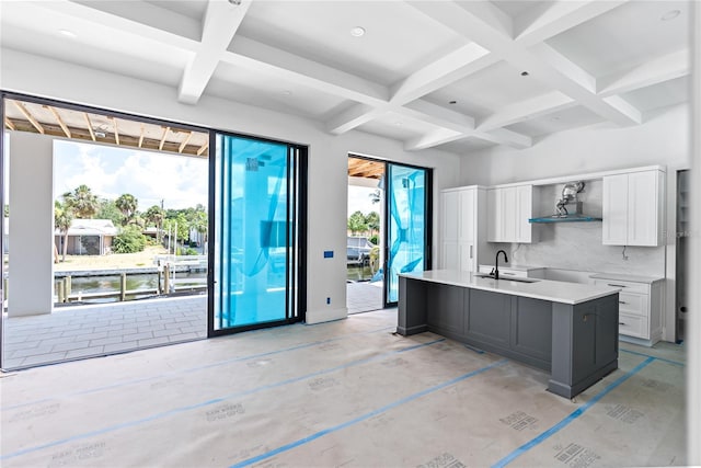 kitchen with coffered ceiling, sink, tasteful backsplash, a kitchen island with sink, and white cabinets