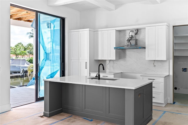 kitchen with sink, an island with sink, white cabinets, decorative backsplash, and beamed ceiling