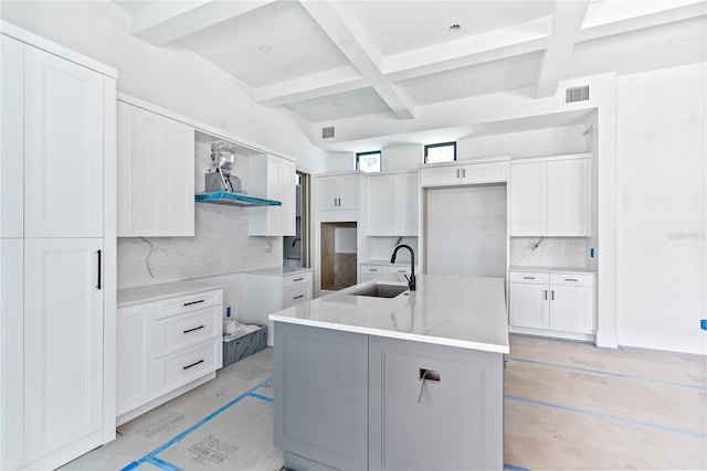 kitchen featuring white cabinetry, sink, decorative backsplash, coffered ceiling, and a kitchen island with sink