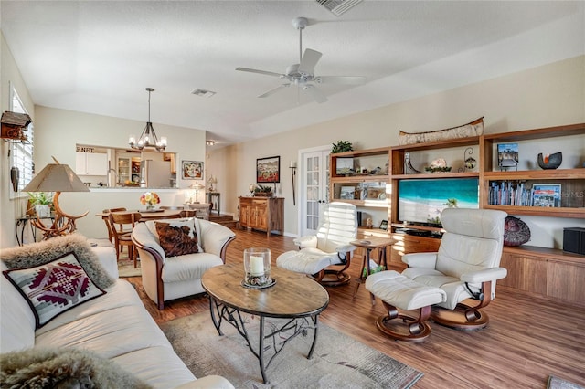 living area featuring ceiling fan with notable chandelier, visible vents, and wood finished floors