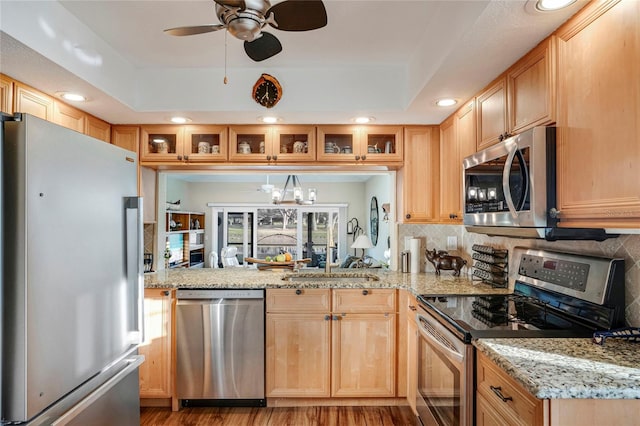 kitchen featuring appliances with stainless steel finishes, a raised ceiling, glass insert cabinets, and backsplash