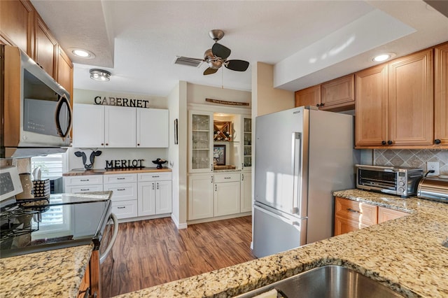 kitchen with a toaster, stainless steel appliances, backsplash, light stone countertops, and light wood-type flooring