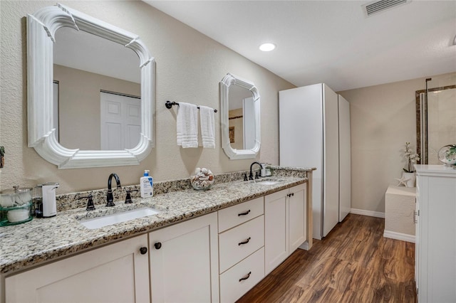 bathroom featuring double vanity, visible vents, a sink, and wood finished floors