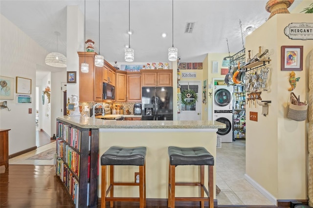 kitchen featuring backsplash, a kitchen breakfast bar, stacked washer / drying machine, black appliances, and kitchen peninsula