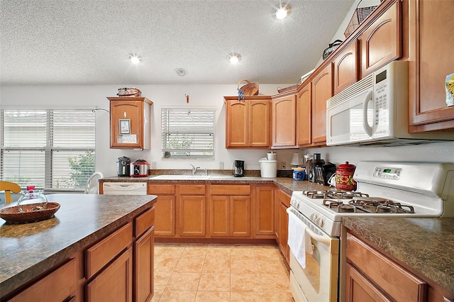 kitchen with light tile patterned flooring, sink, a textured ceiling, and white appliances