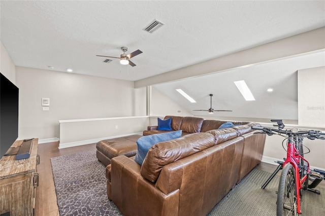 living room with ceiling fan, vaulted ceiling with skylight, a textured ceiling, and dark hardwood / wood-style flooring