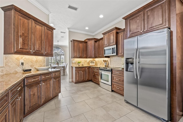 kitchen with pendant lighting, crown molding, stainless steel appliances, light stone counters, and light tile patterned flooring