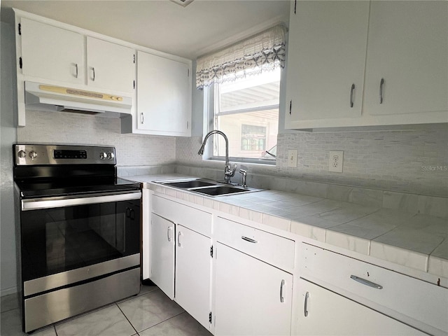 kitchen with electric stove, sink, tile counters, white cabinets, and decorative backsplash