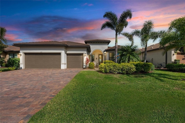 mediterranean / spanish home with decorative driveway, a tile roof, stucco siding, a garage, and a front lawn