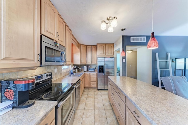 kitchen featuring light brown cabinetry, decorative light fixtures, backsplash, light tile patterned floors, and stainless steel appliances