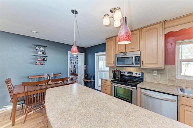 kitchen with backsplash, decorative light fixtures, light brown cabinets, and appliances with stainless steel finishes