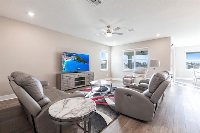 living area featuring visible vents, ceiling fan, light wood finished floors, and a wealth of natural light