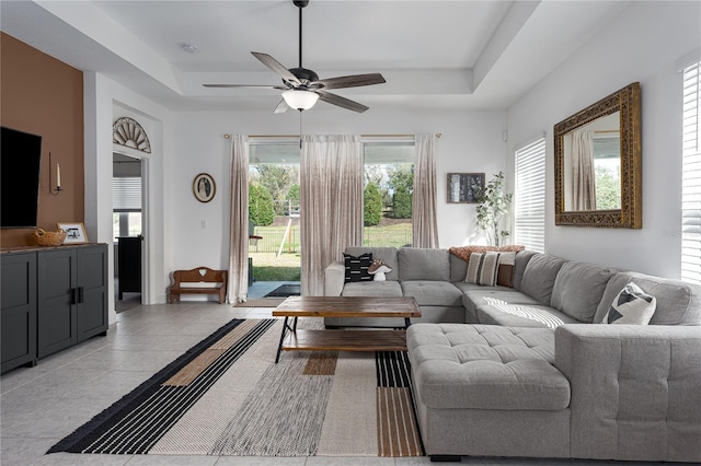 living room featuring a raised ceiling, light tile patterned floors, and ceiling fan