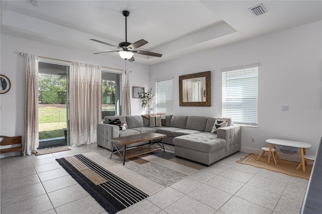 tiled living room with plenty of natural light, a raised ceiling, and ceiling fan