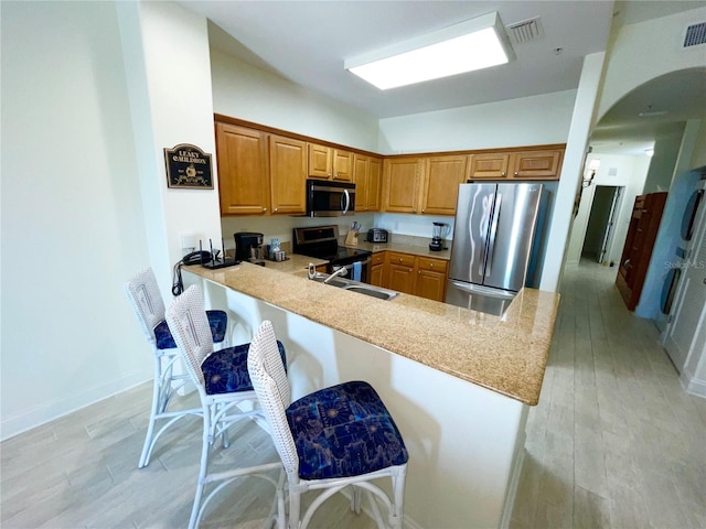 kitchen with visible vents, a breakfast bar area, brown cabinets, a peninsula, and stainless steel appliances