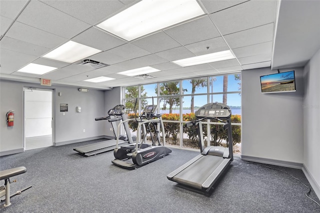 exercise room with a paneled ceiling, baseboards, visible vents, and floor to ceiling windows