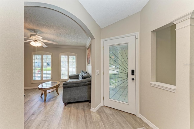 foyer featuring arched walkways, light wood-style flooring, a textured ceiling, and a ceiling fan