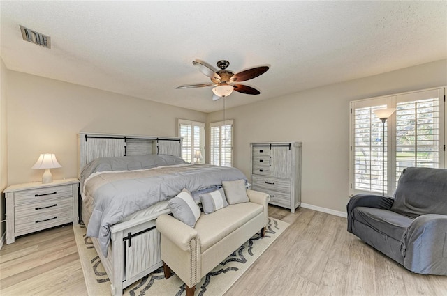 bedroom with visible vents, light wood-style floors, ceiling fan, and a textured ceiling