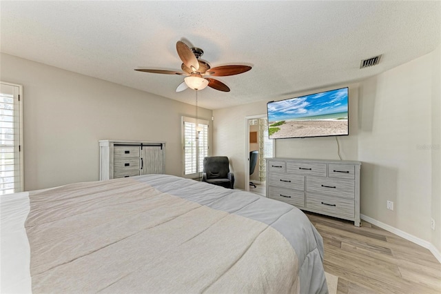 bedroom featuring light wood-type flooring, visible vents, a ceiling fan, a textured ceiling, and baseboards