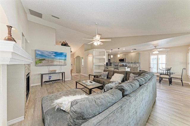 living room featuring a tile fireplace, ceiling fan, a textured ceiling, and light hardwood / wood-style floors