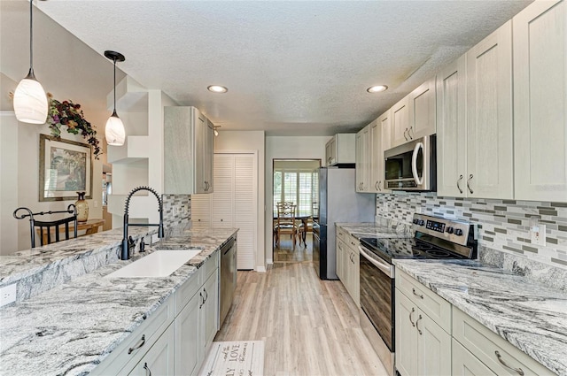 kitchen featuring sink, hanging light fixtures, stainless steel appliances, light stone countertops, and light wood-type flooring