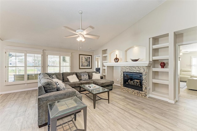 living room with built in features, light wood-style flooring, a tile fireplace, and ceiling fan