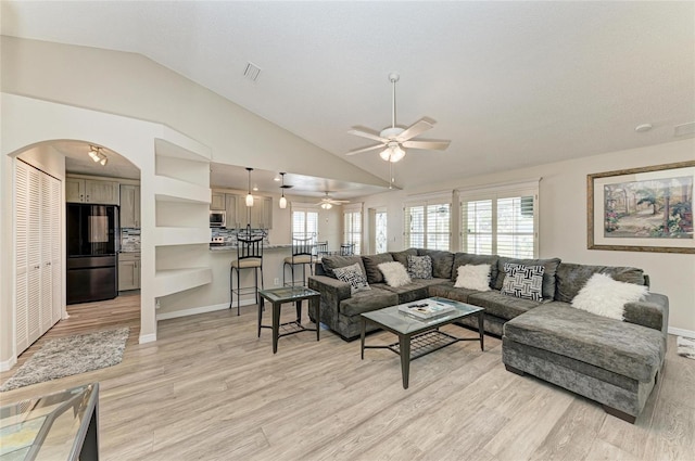 living area featuring visible vents, lofted ceiling, light wood-style flooring, arched walkways, and ceiling fan