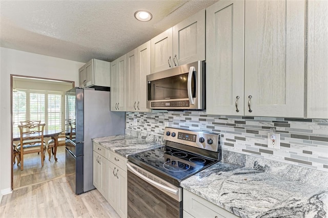 kitchen featuring light stone counters, light wood-style flooring, stainless steel appliances, a textured ceiling, and backsplash