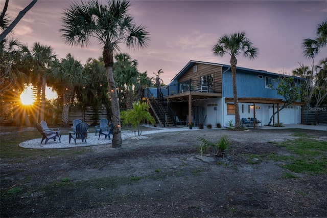 back of property at dusk with stairs, driveway, an outdoor fire pit, and a garage