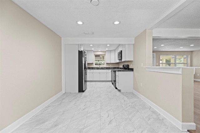 kitchen with appliances with stainless steel finishes, a textured ceiling, and white cabinets