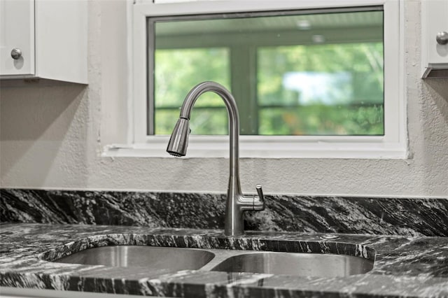 room details featuring dark stone countertops, sink, and white cabinets