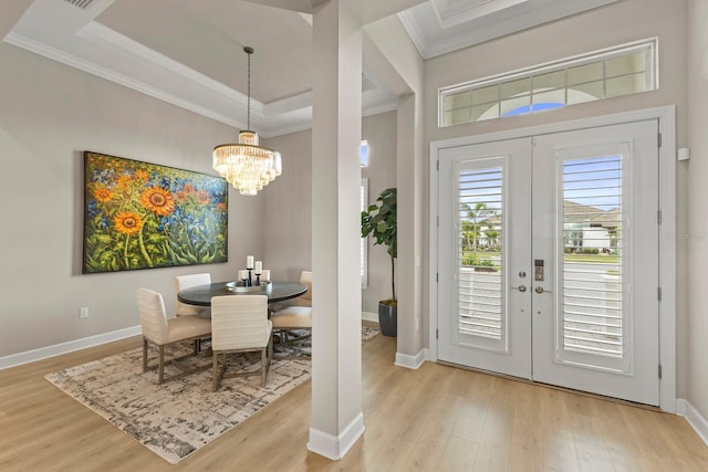 entryway featuring crown molding, a notable chandelier, light wood-type flooring, and french doors