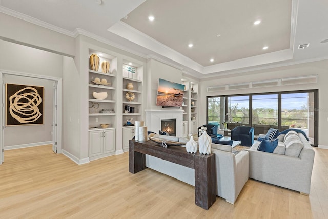 living room with crown molding, a tray ceiling, built in shelves, and light wood-type flooring