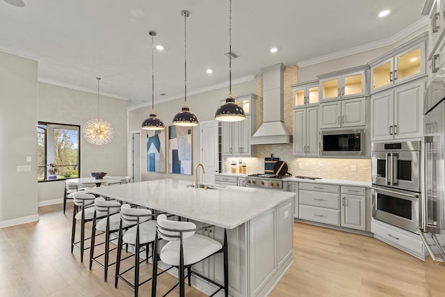 kitchen with built in microwave, sink, a center island with sink, custom range hood, and pendant lighting