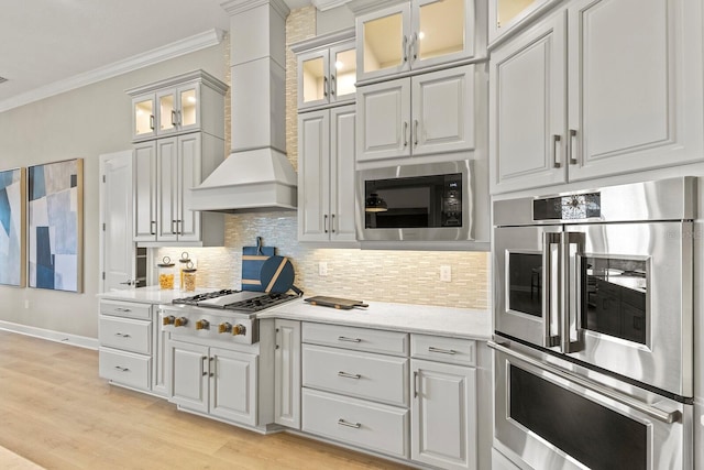 kitchen featuring premium range hood, built in microwave, gas cooktop, crown molding, and stainless steel double oven