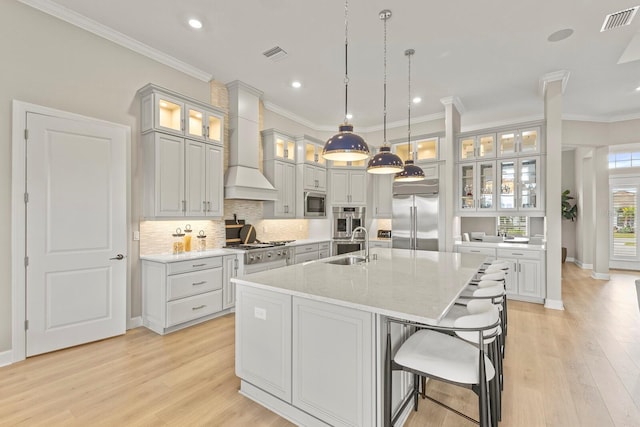 kitchen with sink, a kitchen island with sink, built in appliances, light stone countertops, and custom range hood