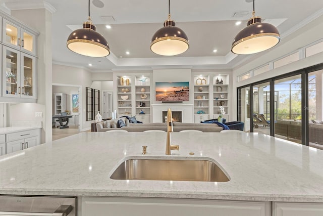 kitchen with pendant lighting, light stone counters, white cabinetry, and a center island with sink