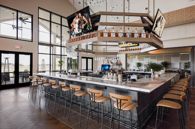 bar featuring ceiling fan, a healthy amount of sunlight, dark parquet flooring, and a high ceiling